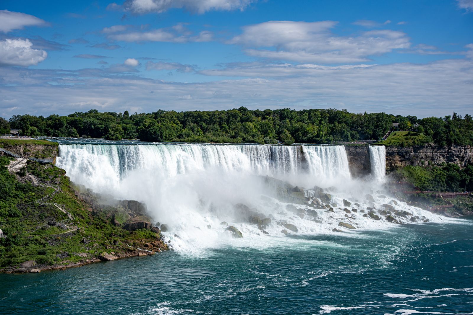 The American Falls pouring over rock into the Niagara River under a blue sky