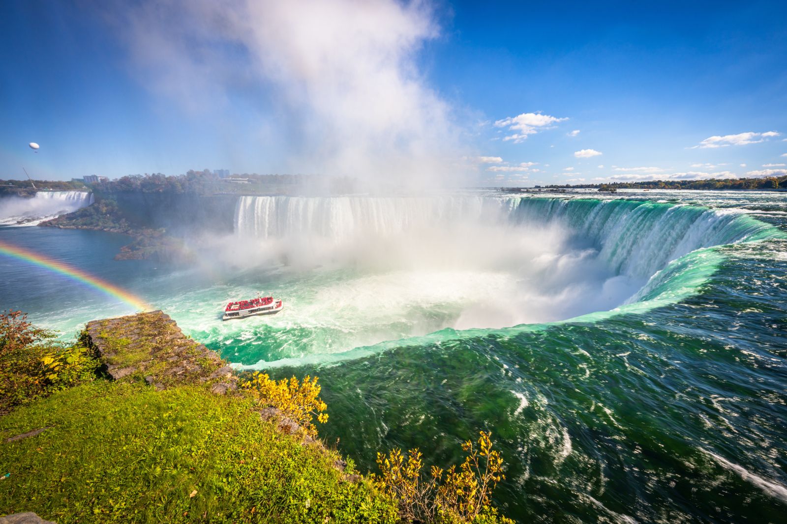 Horseshoe Falls throwing up spray and a rainbow, with a tour boat in the river below